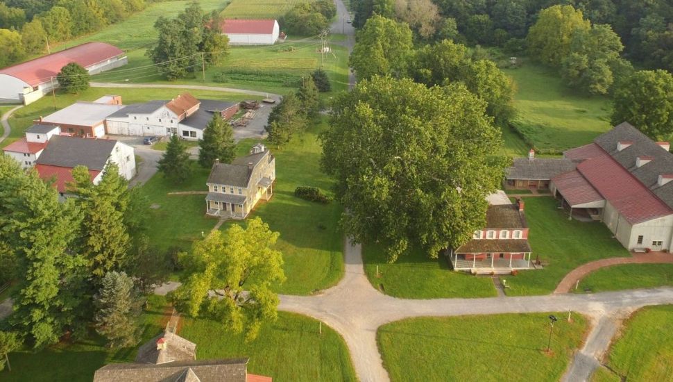 Aerial view of Landis Valley Village & Farm Museum in Lancaster, Pennsylvania, showing historic buildings, barns, tree-lined paths, and surrounding green fields. The image highlights the rural setting and preserved 19th-century architecture central to the museum’s focus on Pennsylvania German heritage.