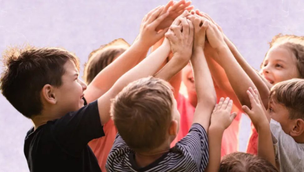 A group of smiling kids huddles with their hands raised toward the center, indicating unity and strength.