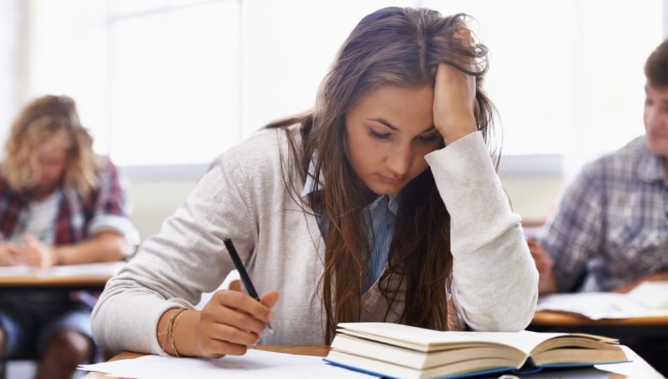 A teenage girl, sitting at a desk, stressed about her exam.