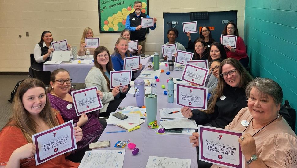 YGBW staff gathered around a table holding their pledges as part of the Five Days of Action® pledge to help keep children safe from abuse.