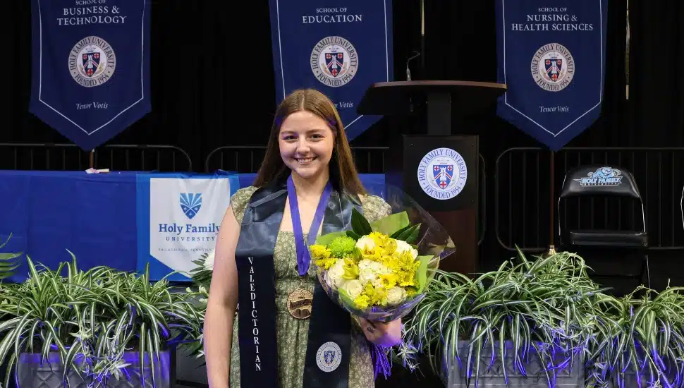 Female college valedictorian smiles and holds yellow flowers.