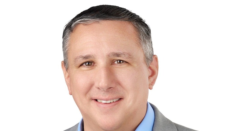 Headshot of middle-aged white male executive in gray suite and blue collared shirt.