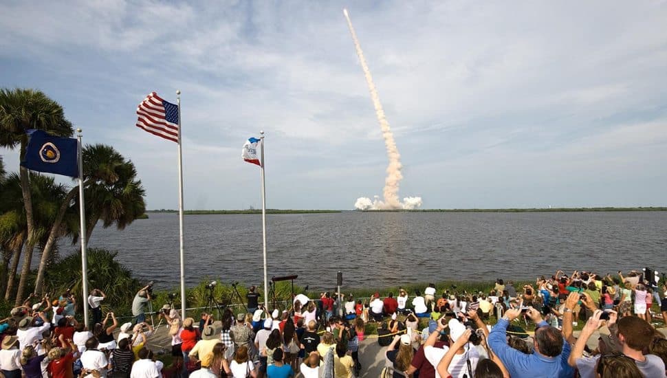 People watching rocket mission launch go into sky.