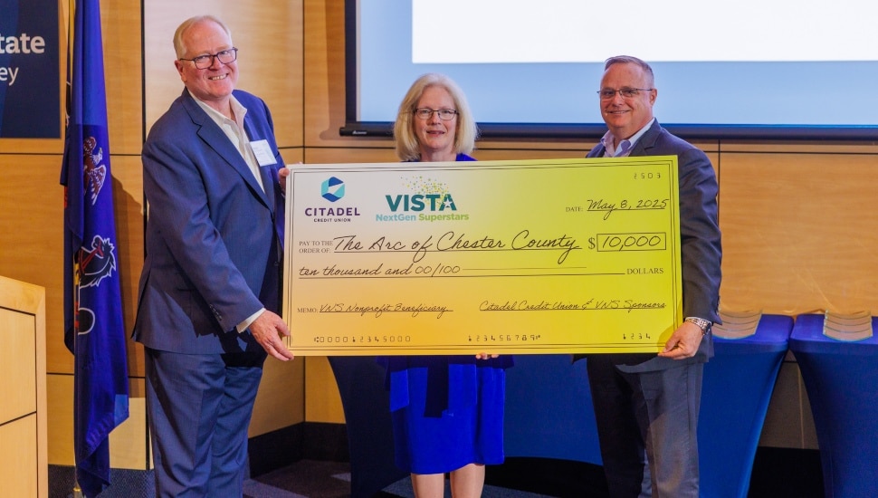 Two male businessmen present a giant check to a nonprofit executive.