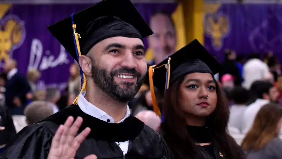 Two DCCC graduates in caps and gowns during the commencement ceremony, smiling and looking ahead amid a crowd of attendees.