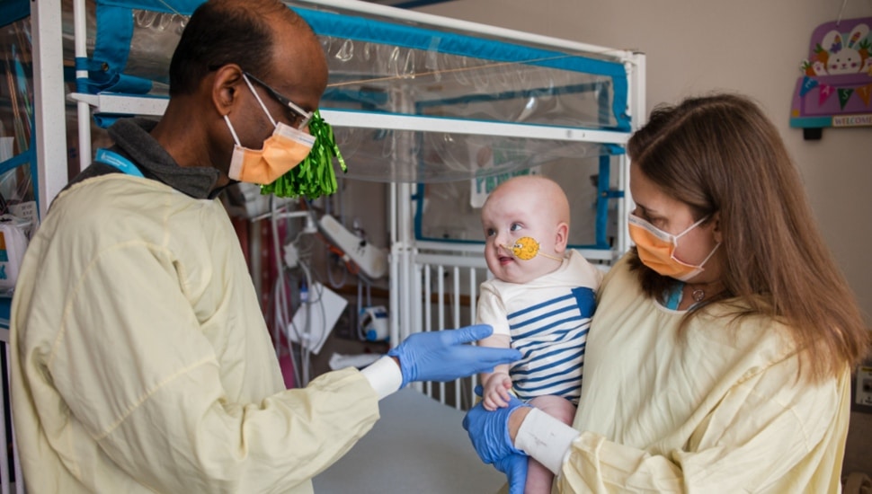 Two doctors in yellow scrubs and facemasks hold baby.