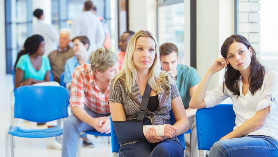 People at ER visit in waiting room sitting on blue chairs.