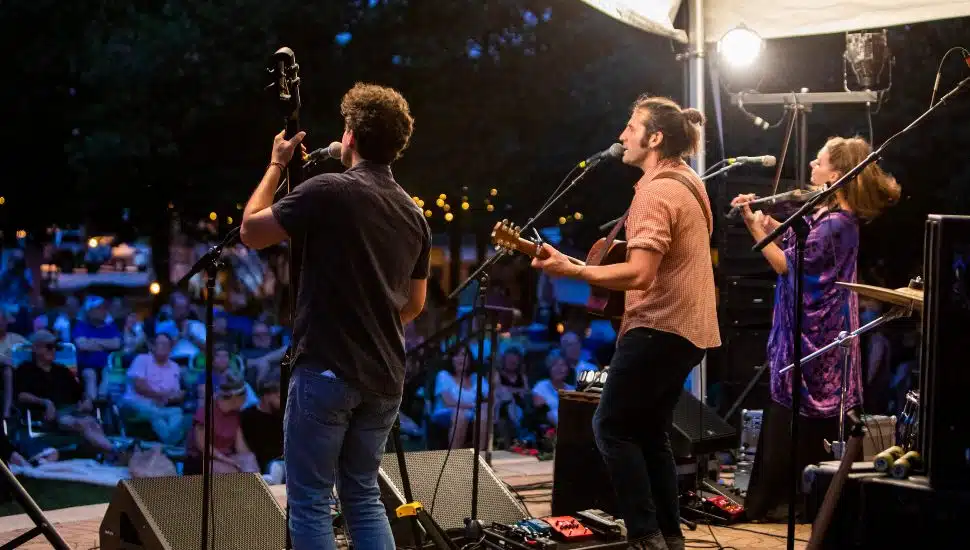 A band on stage performing in front of a large crowd at night.