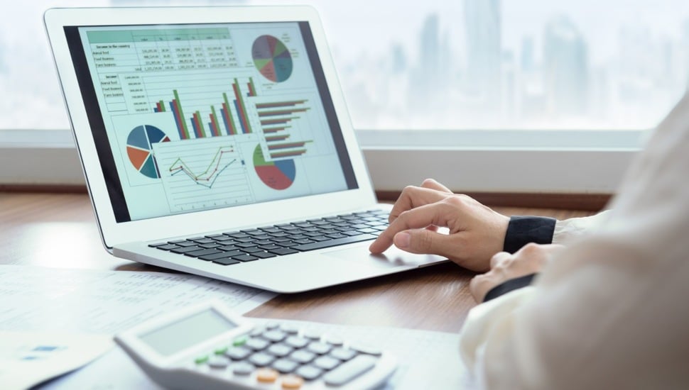 Businessman looks at charts and spreadsheets on a laptop.