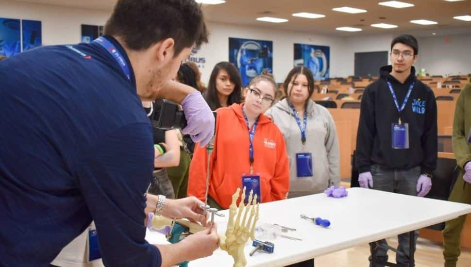 Students from Chester County Futures observe a medical professional demonstrating a surgical procedure on a synthetic bone model during a STEM career day at Globus Medical.