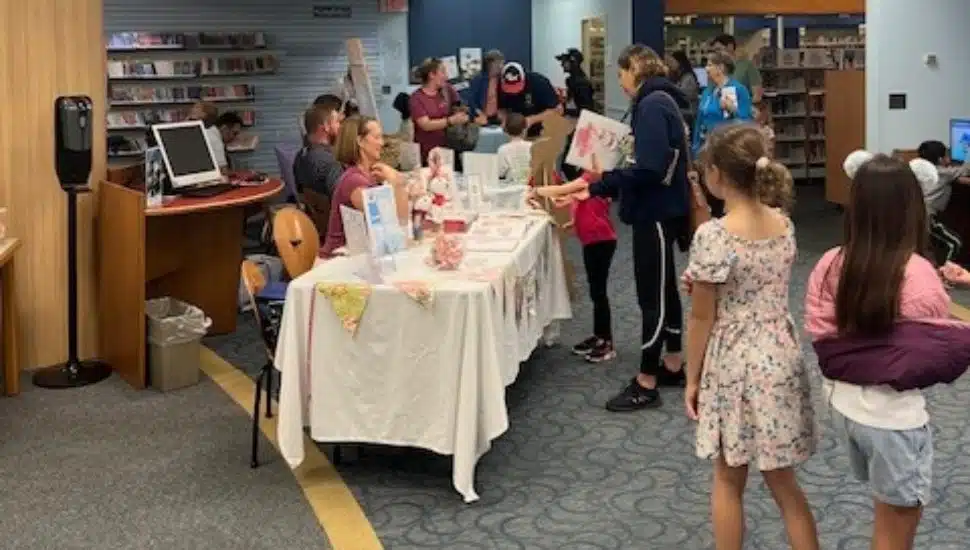Visitors, including children and families, interact with local authors seated behind tables displaying books and promotional materials at the Chester County Library during the “Read Local!” author showcase event.