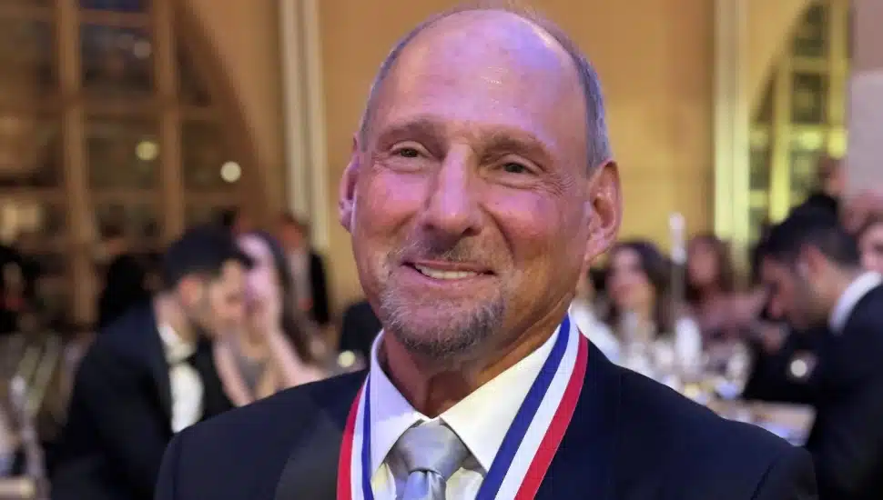 Older banking executive in dark suit and white shirt wears his award medal.