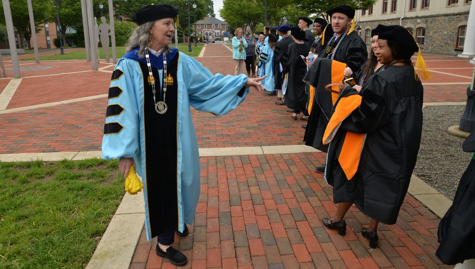 Widener University President Stacey Robertson shares a moment with some of the 2025 graduates who are lined up outside.