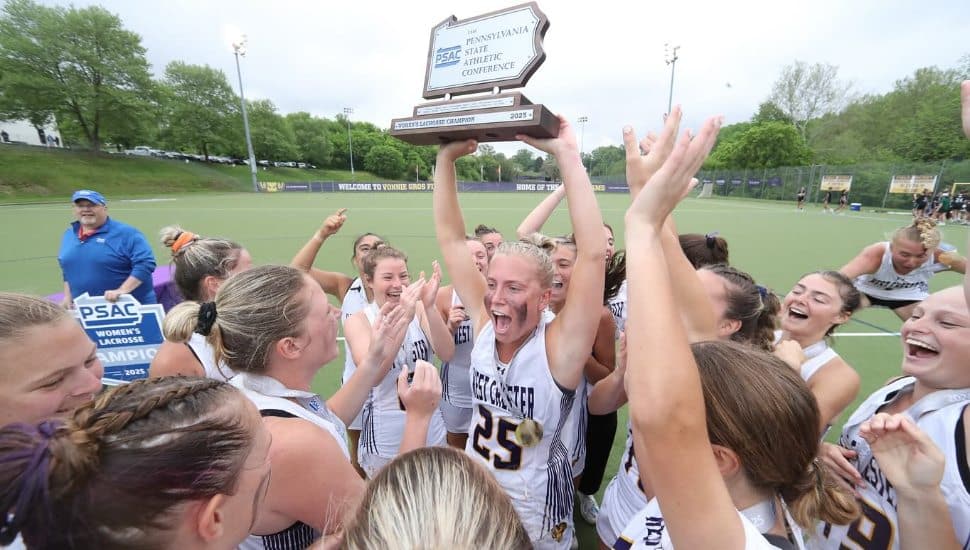 WCU women's lacrosse in white uniforms hold trophy in air while celebrating their win.