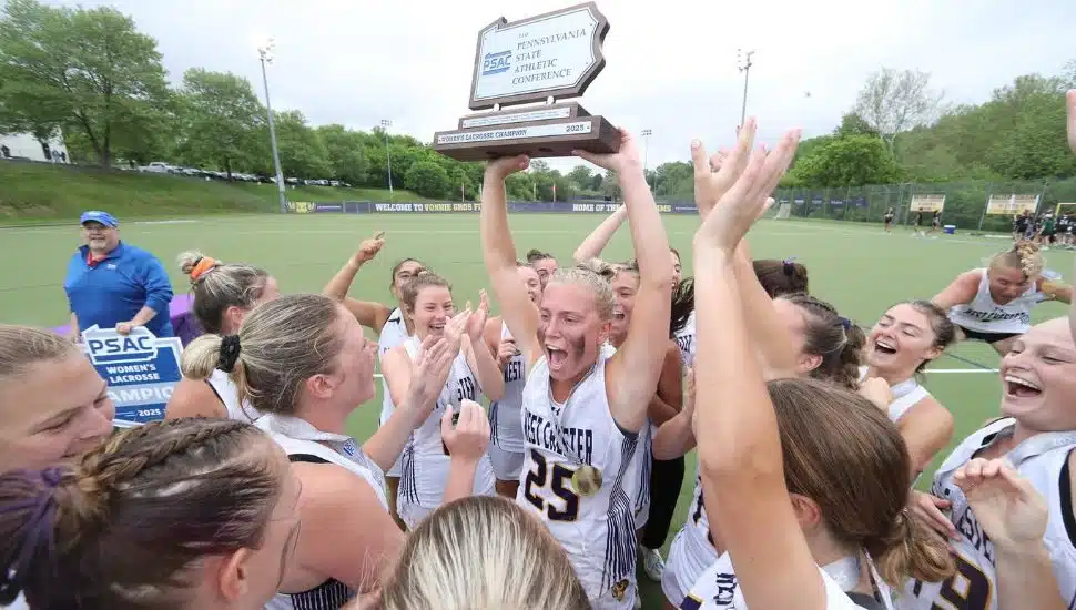 WCU women's lacrosse in white uniforms hold trophy in air while celebrating their win.