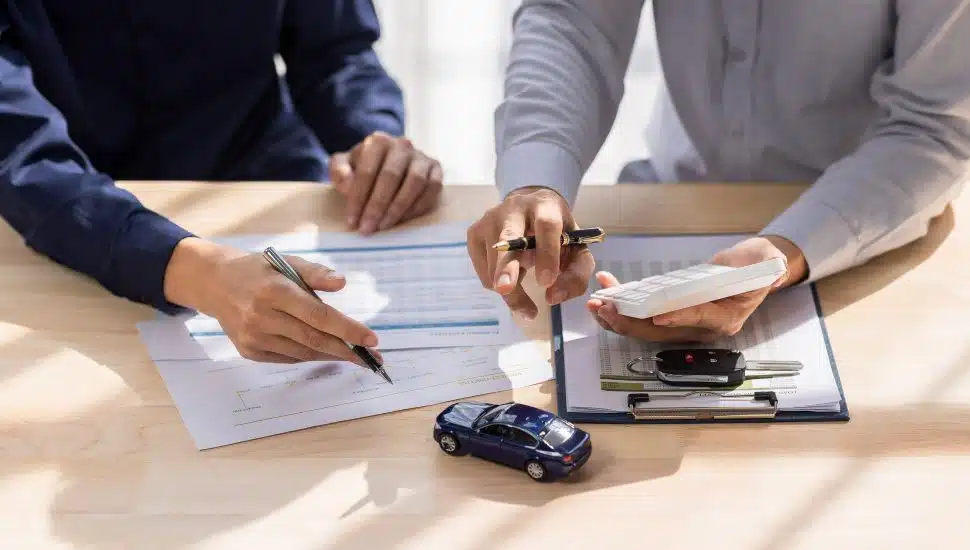 Two people discussing auto insurance with tiny car and papers on table.