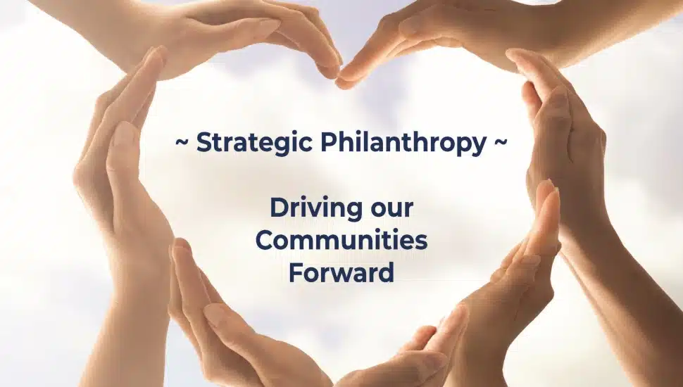 Hands forming a circle around the words “Strategic Philanthropy – Driving our Communities Forward” on a soft neutral background symbolizing collaboration, generosity, and community support.