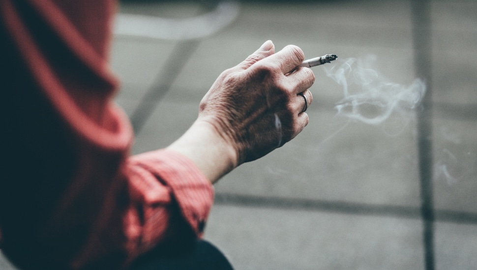A person's hand holding a smoking cigarette.