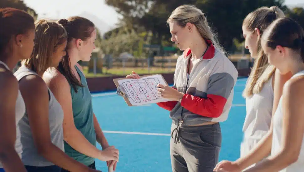 High school coach talking to female athletes at field hockey.