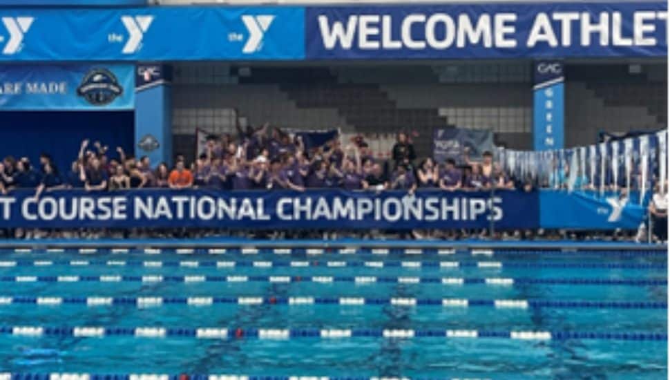 Swimmers and supporters line the pool deck under a banner reading "Short Course National Championships" at the YMCA 2025 Nationals, with vibrant blue lanes in the foreground and a “Welcome Athletes” sign above.