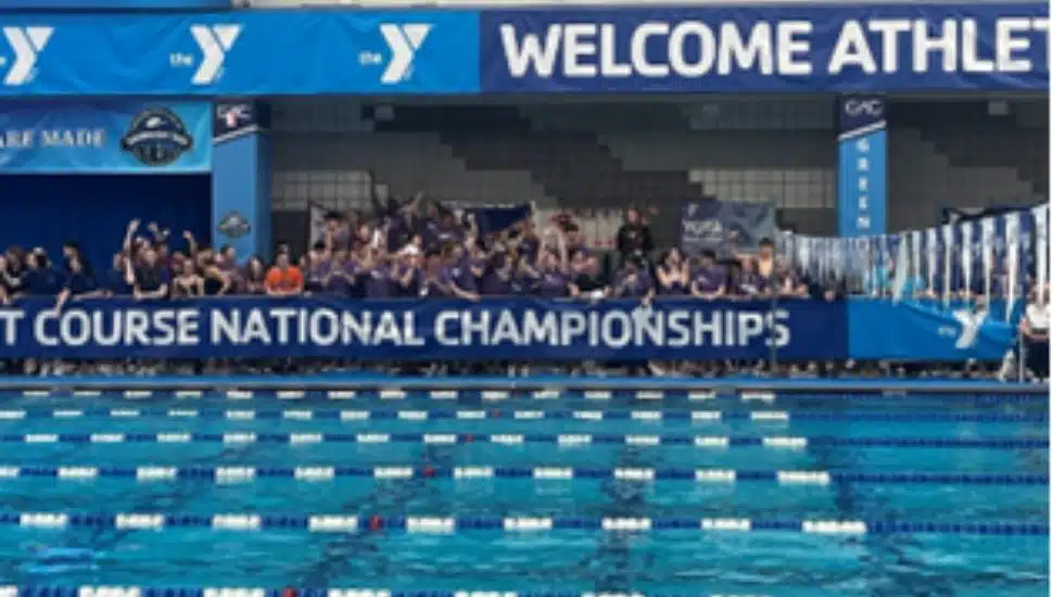 Swimmers and supporters line the pool deck under a banner reading "Short Course National Championships" at the YMCA 2025 Nationals, with vibrant blue lanes in the foreground and a “Welcome Athletes” sign above.