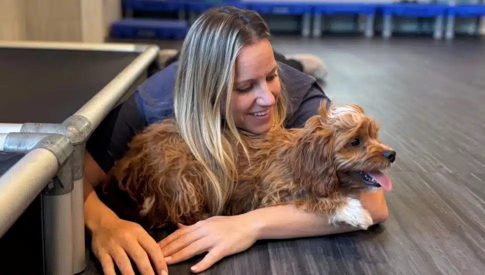 Blond woman hugs her dog while lying on the ground.