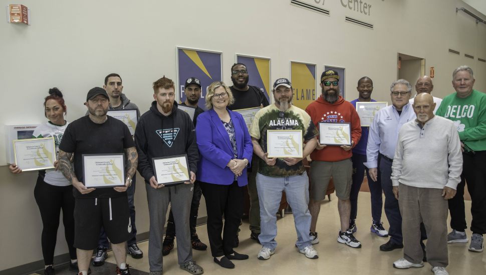 DCCC VP of Workforce Development Karen Kozachyn (center) and (far right) DCCC welding instructors Sal Russomano, Anthony Tullio and Tom Quinn presented certificates to the first cohort of newly trained entry-level welders in the Good Jobs Challenge tuition-free program. Students stand in a line holding their certificates.