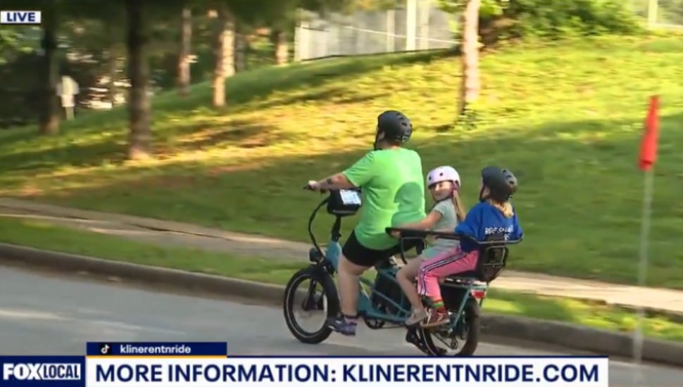 Person and child on e-bike on road.