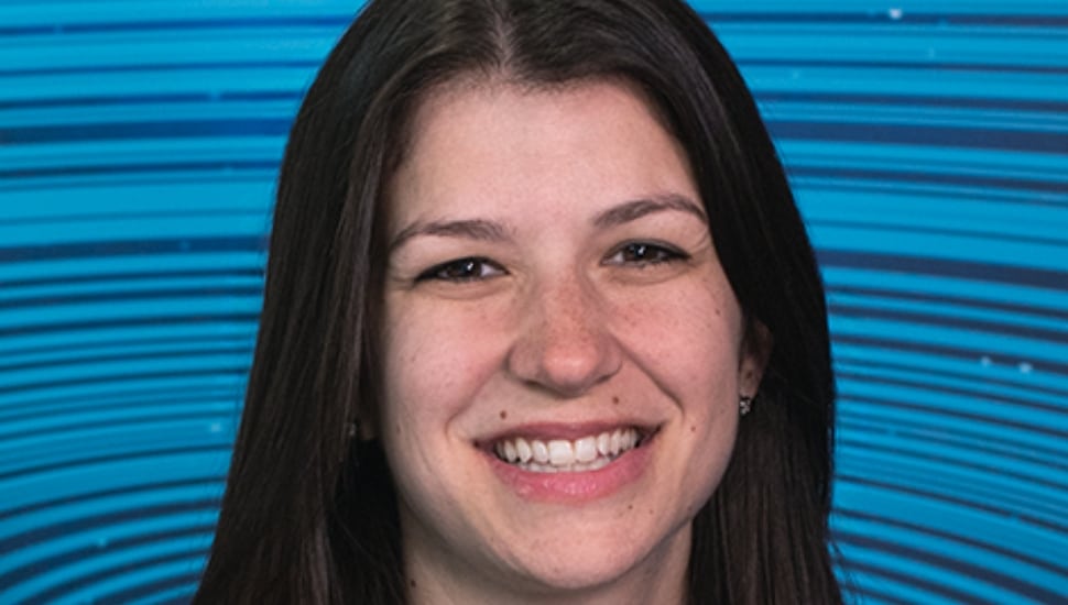 Emily Gatto: She has long dark hair and smiles warmly in front of a vibrant blue background with curved line patterns.