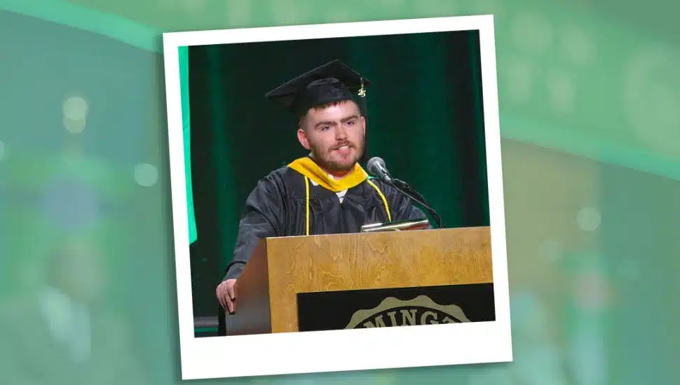Nicholas Phillips stands behind a podium dressed in cap and gown, delivering speech.