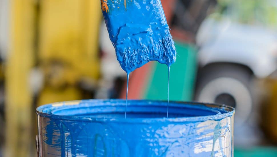 Paint brush dipped into blue paint can.