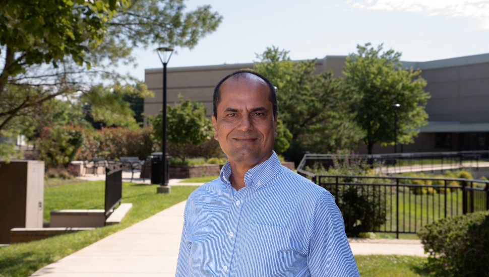 A professional photo of Raghu Sangwan outside Penn State's campus on a sunny day. He wears a light blue shirt and smiles at the camera.