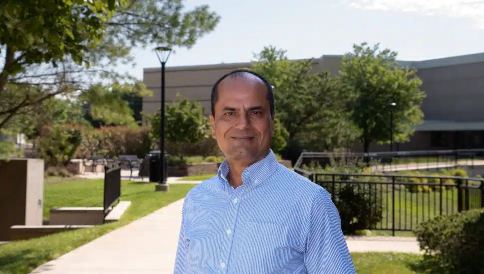 A professional photo of Raghu Sangwan outside Penn State's campus on a sunny day. He wears a light blue shirt and smiles at the camera.