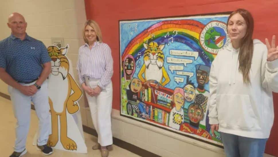 Jacqueline Rose throws up a peace sign as she gifts the painting, seen behind her with Principal Maria Stauffer and Assistant Principal Jeff Kuciapinski.