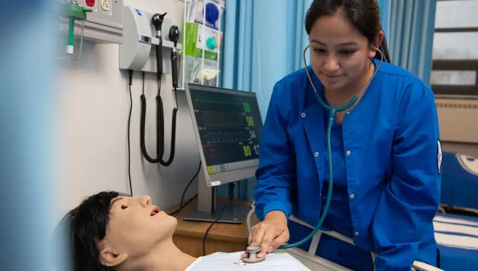 A nursing student in blue scrubs practicing care on a dummy in Immaculata's simulation lab.