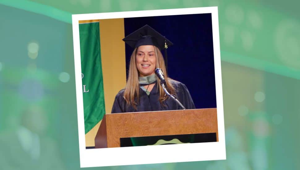 Summer McMenamin in a graduation cap and gown standing at WilmU's podium delivering a speech at the ceremony.