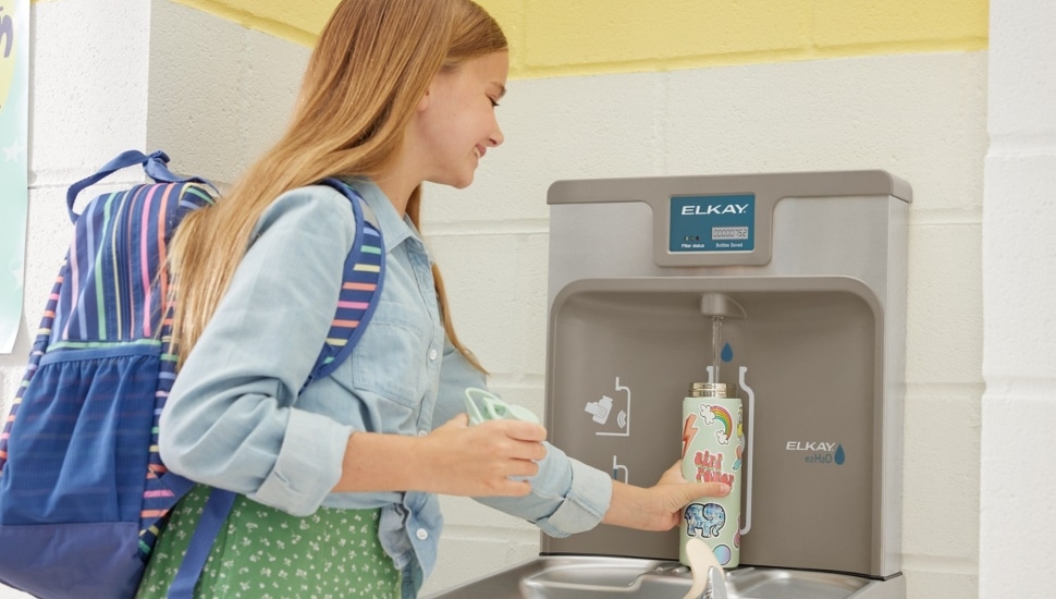 Young girl using water fountain to fill up water bottle.