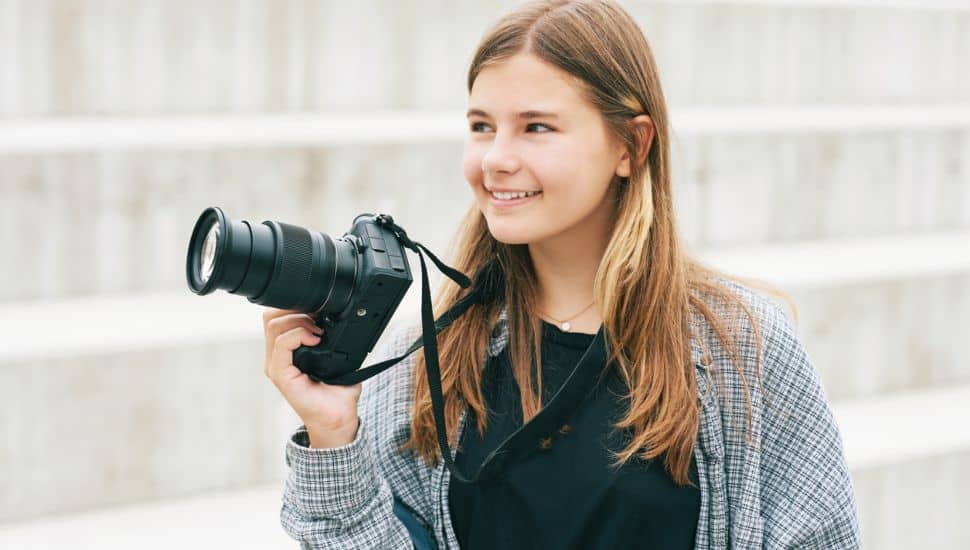 Outdoor portrait of young happy teenage girl holding mirrorless camera.