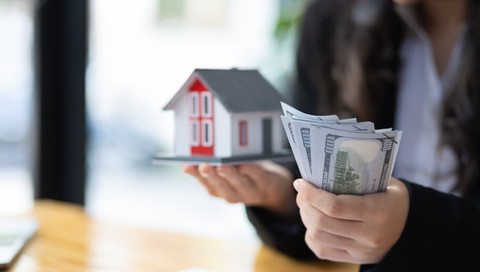 Person holding tiny house and money in one hand for purchase concept.