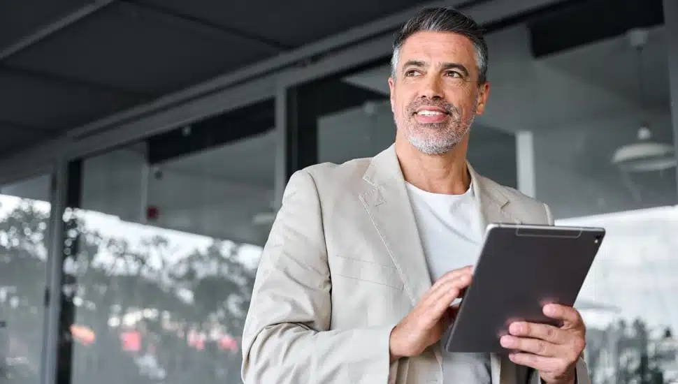 Smiling middle-aged businessman standing outside office holding digital tablet.