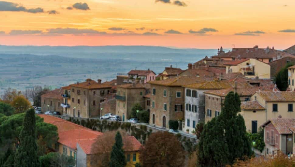 Sunset view over the hilltop town of Cortona, Italy, featuring terracotta rooftops, stone buildings, and rolling countryside in the distance — one of the dream destinations in the People’s Light 50th Birthday Raffle.