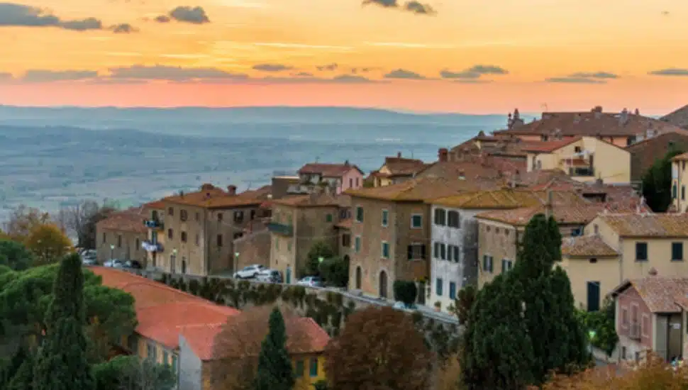 Sunset view over the hilltop town of Cortona, Italy, featuring terracotta rooftops, stone buildings, and rolling countryside in the distance — one of the dream destinations in the People’s Light 50th Birthday Raffle.