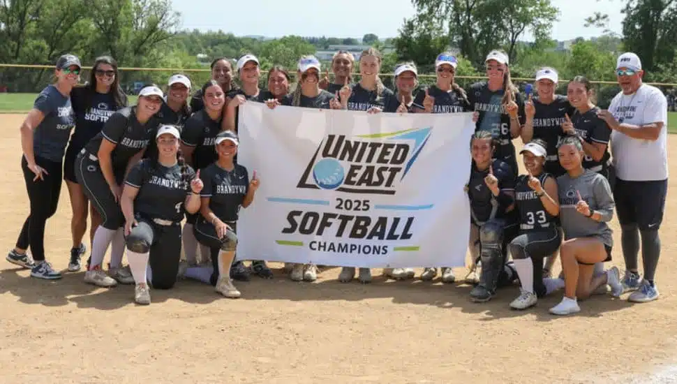 Penn State Brandywine's softball team holds the championship banner on the softball field.