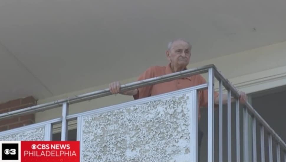 Elderly man looking outside on his balcony.