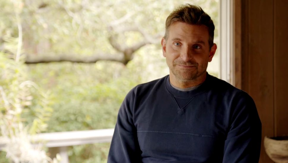 Bradley Cooper in a dark blue shirt, looking ahead.