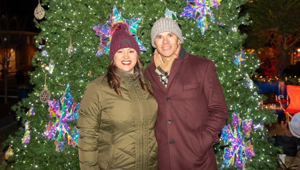 Christmas Parade Emcees Kathy Romano and Adam Joseph with christmas tree behind them.