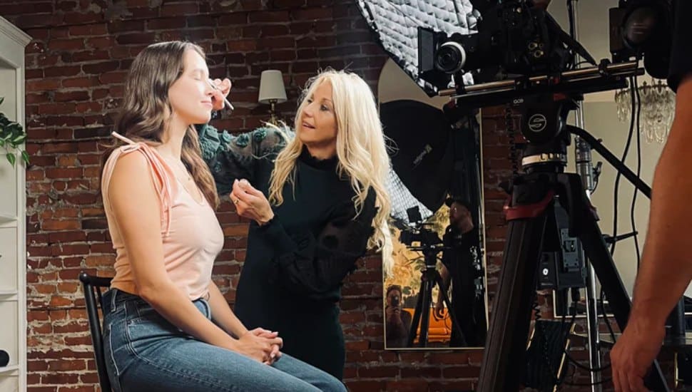 Darci Henry applies makeup to client's face with giant light shining.