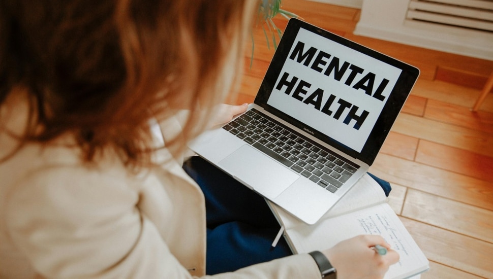 Woman looks at laptop computer with words Mental Health on screen.