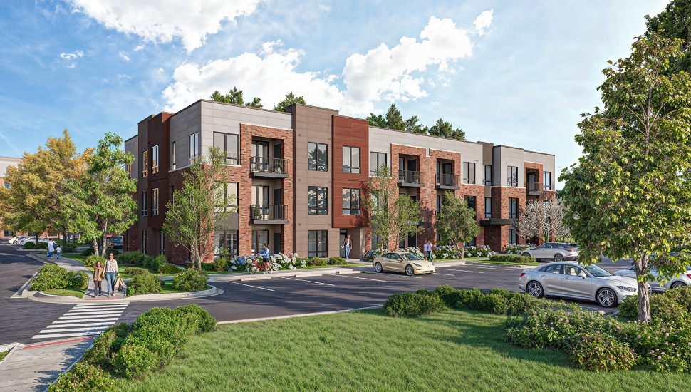 Modern three-story apartment complex with a mix of brick and panel facade, surrounded by landscaped greenery, trees, and a parking lot with several cars. People are walking and biking near the entrance on a sunny day with partly cloudy skies.