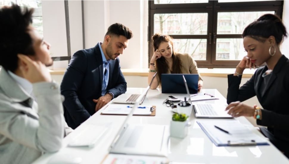 Four young employees with low morale sit detached at a conference room table.